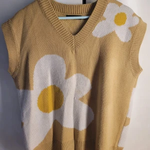 Beige stickad väst med blommönster från Shein - Säljer en superfin beige stickad väst från Shein med stora vita blommor och gula detaljer. Den har en v-ringad hals och är perfekt för vår och sommar. Västen är i mycket bra skick och passar perfekt för en avslappnad och trendig look. 🌼