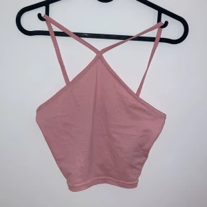 Rosa ärmlös linnetopp - Säljer en söt rosa linnetopp med smala axelband som korsas i ryggen. Toppen är i ett mjukt och bekvämt material, perfekt för sommardagar. Den är i bra skick och passar utmärkt till både vardag och fest. Perfekt att matcha med jeans eller en kjol!