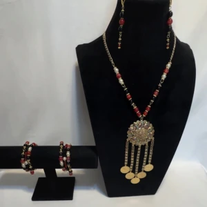 Färgglatt smyckeset med halsband, armband och örhängen - Snyggt smyckeset med ett halsband, armband och örhängen. Halsbandet har en stor, glittrig medaljong med hängande guldfärgade kedjor och färgglada pärlor i rött, svart och guld. Armbanden matchar med liknande pärlor och örhängena har en enkel design med samma färgtema. Perfekt för att liva upp en festoutfit! Ett par örhängen och ett par armband plus en halsband handgjorda mycket mycket fint nytt oanvänd 