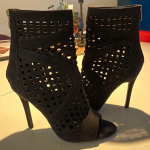 Svarta klackskor med utskuren design - Snygga svarta klackskor med en cool utskuren design som ger en unik look. Perfekta för festliga tillfällen! Skorna har en spetsig tå och dragkedja baktill för enkel på- och avtagning. De är  helt nya och redo att användas för att lyfta din outfit.