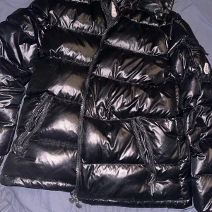 Svart pufferjacka  Moncler som är storlek M helt ny använt en vinter oskadad. - Säljer en snygg svart pufferjacka från Moncler i mycket bra skick. Jackan är perfekt för vintern med sitt quiltade mönster och långa ärmar. Den har en dragkedja framtill och praktiska fickor. Huvan ger extra skydd mot kyla. Perfekt för både vardag och festliga tillfällen!