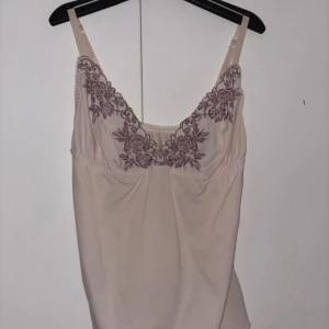 Babyrosa linne med broderade detaljer - Säljer ett elegant beige linne med vackra broderade detaljer! Linnet har justerbara axelband och en mjuk, flytande passform. I mycket bra skick, passar storlek: XS/S