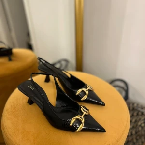 Svarta pumps med gulddetaljer  - Snygga svarta pumps med spetsig tå och gulddetaljer från Zara. Perfekta för en festlig kväll eller en elegant middag. De har en liten klack som ger en bekväm höjd utan att kompromissa med stilen.