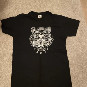 Kenzo t-shirt - Säljer en svart t-shirt från Kenzo med ett coolt tigertryck i vitt och grått på framsidan. Perfekt för en avslappnad stil eller att bära på fest. T-shirten är i bra skick och har en normal passform. Skriv vid minsta lilla fundering✍️😀✅