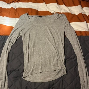 Grå långärmad topp - Säljer en enkel och stilren grå långärmad topp. Perfekt för vardagsbruk eller som basplagg. Den är mjuk och bekväm, med en lätt passform. Passar bra till jeans eller kjol för en avslappnad look.