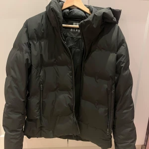 Grön vinter jacka ifrån Uniqlo - Säljer en svart dunjacka från Uniqlo i mycket bra skick. Jackan har en dragkedja framtill och två praktiska fickor med dragkedjor. Perfekt för kalla vinterdagar med sin varma och puffiga design. Den har en hög krage för extra skydd mot kyla. Passar både till vardags och mer avslappnade tillfällen.inga defekter, köpt december 2023