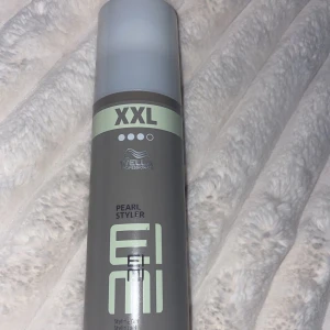 Hårprodukt - Bild på en stylingprodukt från Wella Professionals, EIMI Pearl Styler. Produkten är i en grå flaska med en silverfärgad kork och har XXL-storlek. Perfekt för att skapa textur och glans i håret.