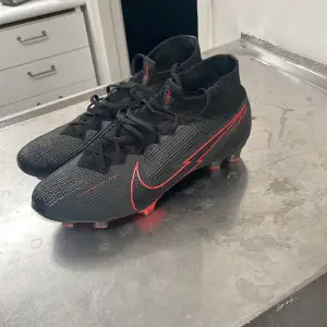 Säljer ett par svart-röda Nike fotbollsskor i mycket bra skick. De har en snygg röd Nike-logga och snörning för perfekt passform. Skorna har en tight passning och är perfekta för fotbollsträning eller match. Sulan har röda detaljer och är designad för optimalt grepp på planen.