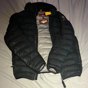 Svart pufferjacka från Parajumpers - Säljer en snygg svart pufferjacka från Parajumpers i mycket bra skick. Jackan har en dragkedja framtill och en cool patch på sidan håller dig varm under sen vinter, vår och höst, stilren. Passar bra till både vardag och festliga tider. Storlek herr M. Passar även bra till S. Skicket är 8/10 med några små vägar där fjädrar kan ta sig ut men annars väldigt bra skick och snygg. Köptes förra hösten så bara ett år gammal t knappt använd, produkten är äkta finns bevis, Scan finns, plus kvitto
