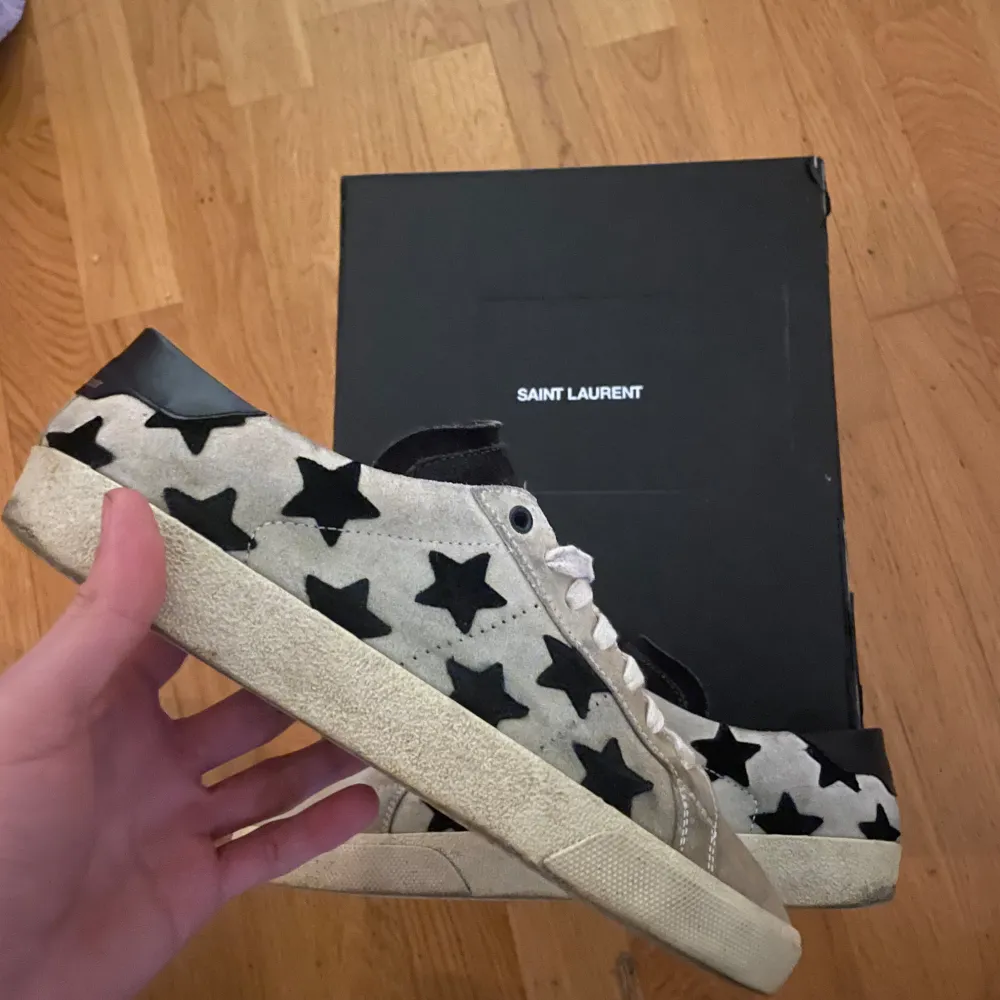 Säljer ett par snygga Saint Laurent sneakers i beige med svarta stjärnor. Skorna har en cool och unik design med snörning och är i bra skick. Perfekta för både vardag och fest! Kommer med originalkartong. Storlek 42.5 men passar 43.5🙌. Skor.