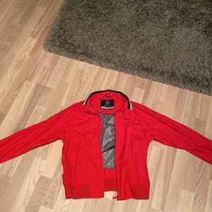 Röd vindjacka från Henri Lloyd - Vindjacka från Henri Lloyd. Knappt använt och den är i stort sett helt perfekt (lite slit på remmen från att den bara hängt på en krok). Den är perfekt när det blåser och när det är lite kyligt. Pris kan diskuteras 