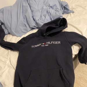 Säljer en snygg och bekväm mörkblå hoodie från Tommy Hilfiger. Den har en klassisk design med loggan broderad på bröstet och en praktisk magficka. Perfekt för kyliga dagar eller som en stilren vardagströja. Hör av dig vid intresse!