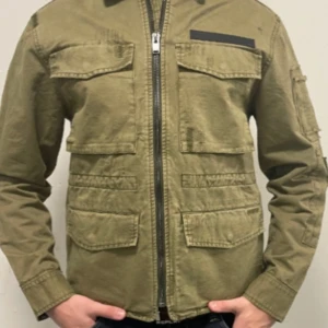 Olivgrön jacka från Zadig & Voltaire - Säljer en snygg olivgrön jacka från Zadig & Voltaire. Den har en cool militärinspirerad stil med flera fickor och dragkedja framtill. Perfekt för höst och vår! Jackan är i mycket bra skick och går för cirka 4000 kr ny. Modellen på bilden är 190 cm lång.