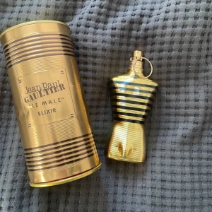 Jean Paul Gaultier Le Male Elixir - Säljer en lyxig parfymflaska från Jean Paul Gaultier, Le Male Elixir. Flaskan har en cool design i form av en manlig torso i guld och svart. Den kommer i en matchande guldig metallförpackning. Perfekt för den som vill ha en elegant och maskulin doft.