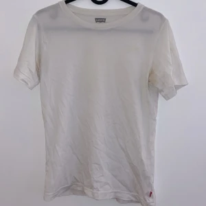 Vit t-shirt från Levi's - Säljer en klassisk vit t-shirt från Levi's i bomull. Den har en normal passform och korta ärmar, perfekt för vardagsbruk. T-shirten är i bra skick och har den ikoniska Levi's-loggan vid nederkanten. Passar till allt och är ett måste i garderoben!