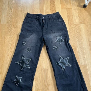 Svarta byxor med stjärndetaljer - Säljer ett par svarta byxor i storlek XL med coola stjärndetaljer. Byxorna har en loose passform och är tillverkade av 80% bomull och 20% polyester. Perfekta för en avslappnad stil med en twist. De har en knapp och dragkedja framtill. Dom e ifrån temu