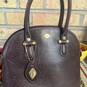 Brun handväska från I Santi - Säljer en elegant brun handväska från I Santi, tillverkad i Italien. Väskan har en stilren design med en texturerad yta och guldfärgade detaljer.