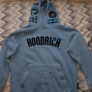 Blå HOODRICH Hoodie (M) - En blå äkta HOODRICH Hoodie med ordet Hoodrich på luvan och bröstet.