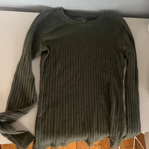 Olivgrön ribbad tröja - Säljer en snygg olivgrön ribbad tröja som är perfekt för höst och vinter. Den har långa ärmar och en rund halsringning. Tröjan är både stilren och bekväm, perfekt för vardagsbruk!