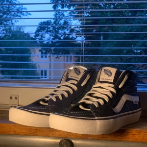Vans Pro Classics sneakers - Säljer ett par snygga Vans Pro Classics Sk8-High sneakers i mörkblått och vitt. Skorna har en klassisk design med den ikoniska vågiga sidostripen och 'Off the Wall'-loggan på hälen. De är gjorda i slitstarkt material och har en bekväm passform med snörning. Perfekta för både vardag och skate! Skorna är i nyskick.