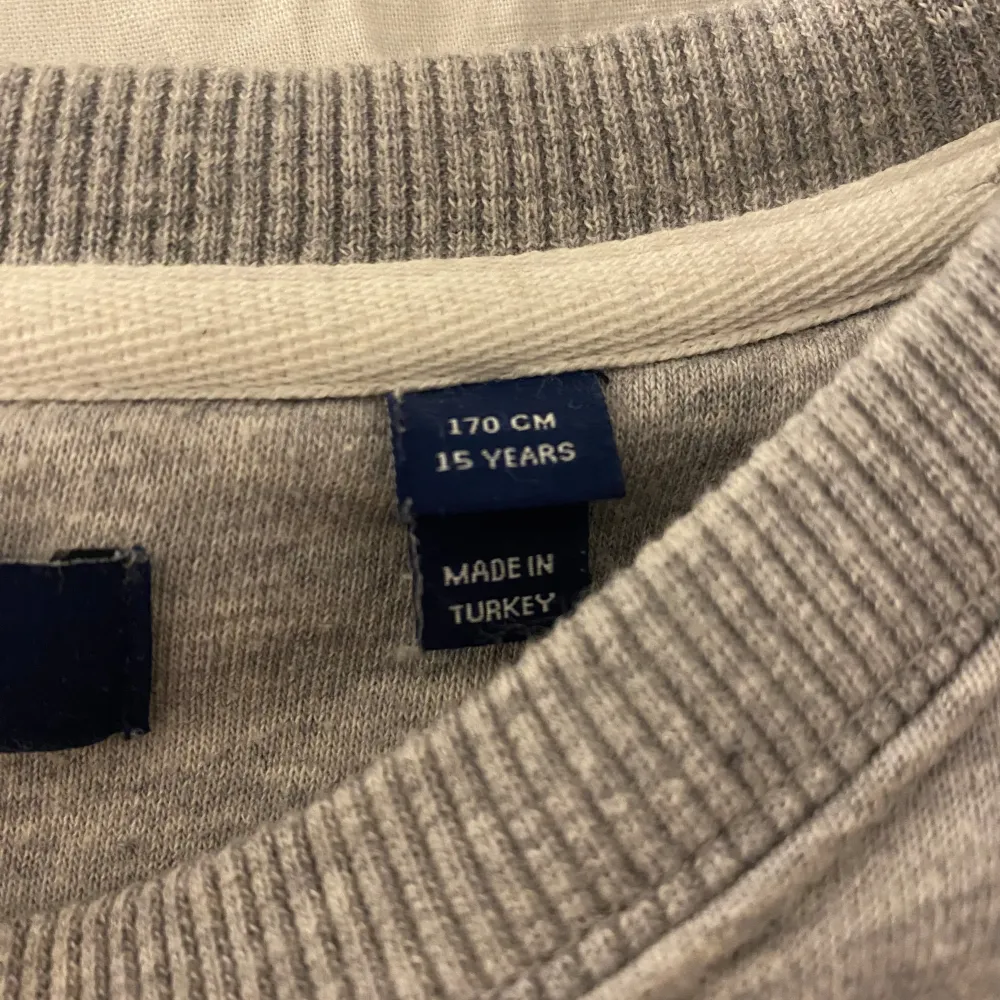 Säljer en stilren och bekväm grå sweatshirt från GANT. Den har ett broderat märke på bröstet och är perfekt för både vardag och chill. Tröjan är i bra skick och passar perfekt för höst och vinter. Den är gjord i mjukt material och har ribbade muddar vid ärmslut och nederkant.. Neuletakit & Villapaidat.