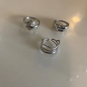 silverringar - Säljer tre snygga silverringar med olika design. En av ringarna har texten 'DUMP HIM' ingraverad, vilket ger en kaxig touch. De andra två ringarna har en stilren och modern design med vågiga och öppna former. Perfekta för att ge din outfit lite edge!