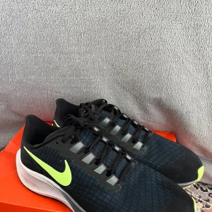 Svarta Nike löparskor med limegröna detaljer - Säljer ett par snygga och sportiga Nike löparskor i svart med limegröna detaljer. Skorna har en bekväm passform med snörning och en vit sula som ger bra stöd under löpningen. Perfekta för träning och vardagsbruk!
