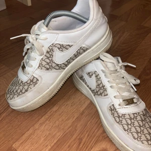 Nike Air Force med mönster - Säljer ett par Nike Air Force med unikt mönster. Skorna är vita med ett snyggt grått mönster på sidorna och framtill. De har klassisk snörning och är i bra skick. Perfekta för både vardag och fest!