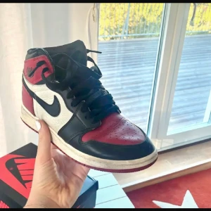 Nike Air Jordans i svart, röd och vit - Säljer ett par klassiska Nike Air Jordans i färgerna svart, röd och vit. Skorna har en snygg design med snörning och den ikoniska Nike-loggan på sidan. Perfekta för både vardag och fest!