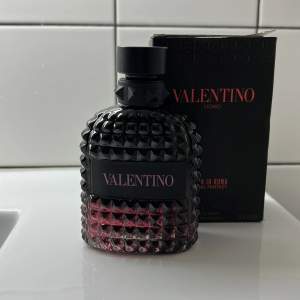 Säljer en lyxig parfym från Valentino, 'Uomo Born in Roma Coral Fantasy'. Flaskan är riktigt snygg med en mörk, nabbig design och en hint av rosa som syns genom glaset. Den har en elegant svart kork och kommer i en stilren svart kartong med röd text. Perfekt för den som vill ha en doft som sticker ut!