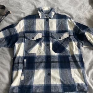 Rutig overshirt från Zara - Säljer en snygg rutig overshirt/jacka från Zara i blått och vitt. Den har en avslappnad passform med långa ärmar och knappar framtill. Perfekt för höst och vår, och funkar både som jacka och skjorta. 