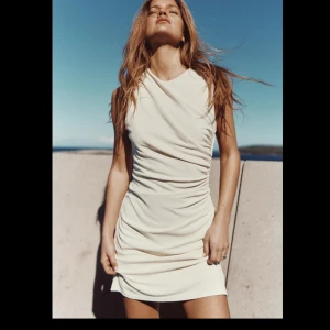 Beige ärmlös klänning - Säljer en superfin beige ärmlös klänning med draperad design. Den är perfekt för sommarens alla fester och har en tight passform som framhäver figuren. Klänningen är gjord i ett mjukt och bekvämt material, vilket gör den både stilren och skön att bära.