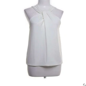 Vit ärmlös topp - Snygg och stilren vit ärmlös topp med en elegant knutdetalj vid halsen. Perfekt för både vardag och festliga tillfällen. Toppen har en lös passform och är gjord i ett mjukt och bekvämt material. den är aldrig använd och har till och med prislappen kvar💞