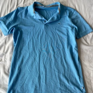 Blå pikétröja från Calvin Klein - Säljer en snygg blå pikétröja från Calvin Klein Golf. Tröjan är i bra skick och har en klassisk krage med knappar. Perfekt för både vardag och sportiga aktiviteter. Den är tillverkad i ett mjukt och bekvämt material. Frågor? Skriv!