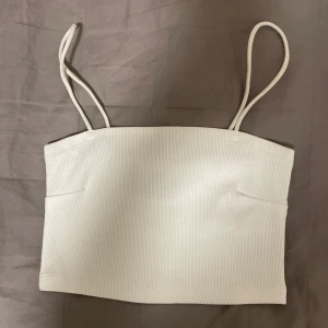 Vit ribbad linnetopp från Gina Tricot - Säljer en vit ribbad linnetopp från Gina Tricot. Toppen har smala axelband och en enkel design som passar perfekt till sommaren. Den är i storlek S och är bekväm att bära.