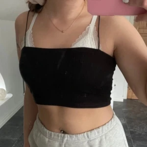 Svart ribbad croppad topp - Säljer en svart ribbad croppad topp med smala axelband. Perfekt för sommaren och kan stylas med olika outfits. Toppen är tight men stretchig och har en enkel men stilren design.