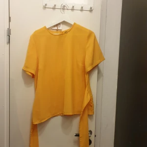 Gul kortärmad topp - Säljer en snygg gul topp med korta ärmar. Den har en unik design med ett knytband som man kan välja att knyta fram eller bak. Perfekt för sommardagar eller en färgglad festoutfit!💛 från bubbleroom, märkt 42 men jag uppskattar den som en M/L