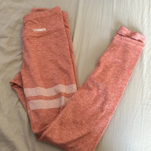 Rosa leggings från Stronger - Säljer ett par snygga rosa leggings från Stronger. De är högmidjade och perfekta för träning. Materialet är mjukt och stretchigt, vilket gör dem superbekväma. De har ett coolt mönster med vita prickar och ränder runt benen. Perfekta för gymmet eller en löprunda!