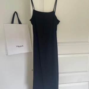 Svart långklänning - Säljer en elegant svart långklänning. Klänningen är ärmlös med smala axelband och har en stilren design. Perfekt för festliga tillfällen eller en kväll ute. Materialet känns mjukt och bekvämt mot huden. Axelbandens sömmar har gått sönder lite.