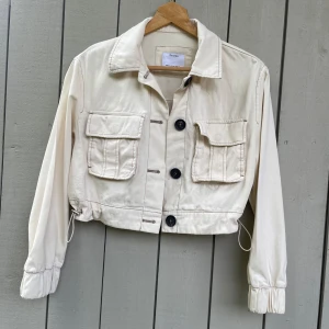 Kort beige jacka - Fin kort beige jacka från Bershka. Storlek xs. Passar även xxs-s bra.  Precis tvättad och ser ut som ny! Material likt en tunnare jeansjacka. Dragsko i midjan och magnet i fickorna. 