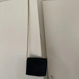 Svart partyväska - Mindre partyväska från & other stories. Fint läder, i gott skick. Vissa missfärgningar på det guldiga bandet. Kan bäras crossbody, eller som clutch eller på axeln. Bandet går att vira för att göra det kortare så att den kan bäras på axeln 