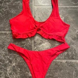 Röd bikini med volangdetaljer - Säljer en superfin röd bikini med volangdetaljer. Toppen har en söt volangkant och en knut framtill som ger en extra touch. Perfekt för sommarens alla stranddagar! 💃