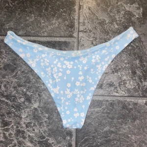 Blå blommig bikiniunderdel - Säljer en superfin ljusblå bikiniunderdel med sött blommönster i vitt. Perfekt för sommardagar på stranden eller vid poolen. Den har en normal passform och är i nyskick. Passar perfekt för dig som älskar en fräsch och somrig stil!
