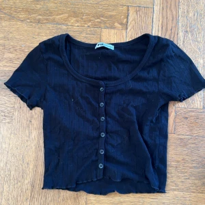 Svart ribbad topp från FB Sister - Säljer en svart ribbad topp från FB Sister i storlek XS. Den har korta ärmar och knappar framtill. Perfekt för en casual look eller att styla upp för fest. Toppen är i bra skick och superbekväm!
