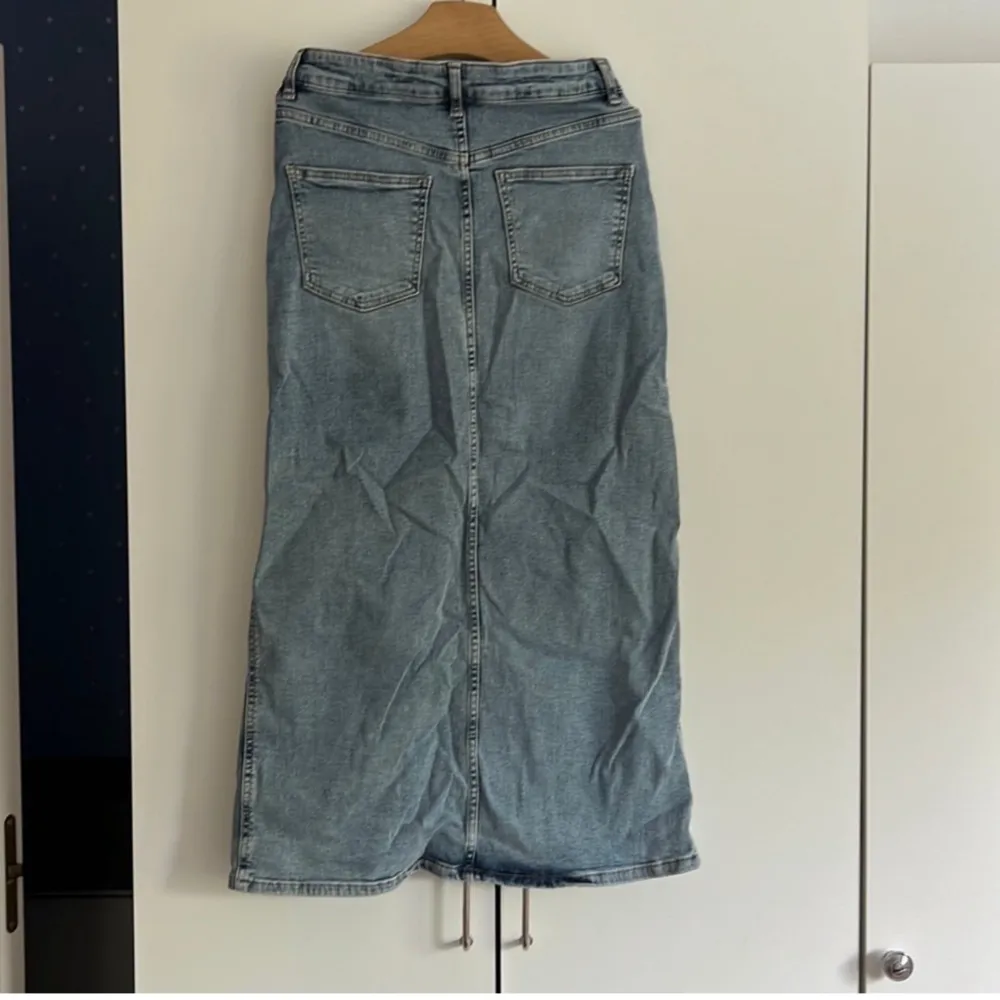 En blå denimkjol med en slits i fram från Kappahl i storlek 34. Kjolen har en hög midja och är i en rak modell. Använd vid fåtal tillfällen. Kjolar.