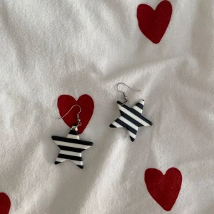 Svartvita randiga stjärnörhängen - Säljer ett par supercoola örhängen i form av stjärnor med svartvita ränder. De är perfekta för att ge en edgy touch till vilken outfit som helst. Örhängena är lätta och bekväma att bära hela dagen. Perfekta för både vardag och fest!