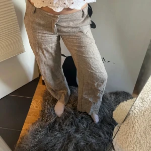 Beige linnebyxor - Säljer ett par snygga herringbone byxor från Designbysi. De har en loose passform och är perfekta för en avslappnad stil. Byxorna har knappar och dragkedja framtill, vilket ger en klassisk look. Perfekta för vår och höst!