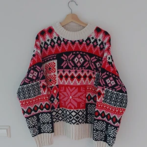 Färgglad stickad tröja från H&M - Säljer en superfin och mysig stickad tröja från H&M i storlek M. Den har ett färgglatt mönster i rött, rosa, svart och vitt med olika geometriska former och stjärnor. Perfekt för kalla dagar och ger en härlig vinterkänsla. 