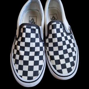 Svartvita rutiga slip-on sneakers från Vans - Säljer ett par klassiska Vans slip-on sneakers med svartvitt rutmönster. De är i välanvänt skick men fortfarande snygga.