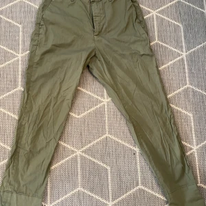 Olivgröna byxor från Hope - Säljer ett par olivgröna byxor från Hope i modellen 'News Trouser'. De är tillverkade i 97% bomull och 3% elastan, vilket gör dem både bekväma och lite stretchiga. Byxorna har en klassisk design med fickor och bälteshällor, perfekta för både vardag och lite mer uppklädda tillfällen.